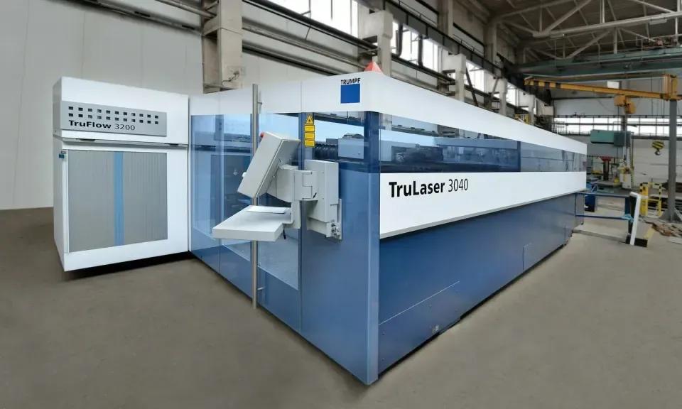 Une grande machine de découpe laser industrielle bleue et blanche avec une enceinte de sécurité vitrée dans un hall industriel