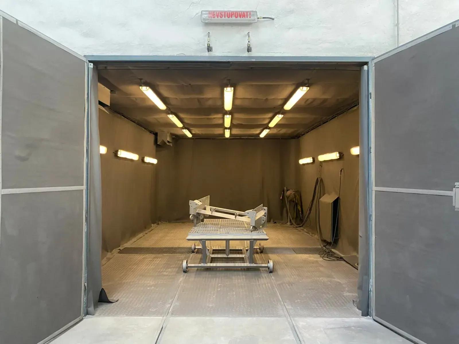 Un châssis de machine en acier soudé sur un support à roulettes, dans une cabine industrielle aux parois en tissu et à l'éclairage zénithal