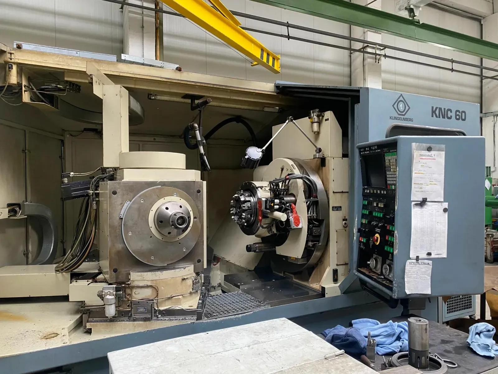 Grande machine de taillage d'engrenages bleue et crème dans un atelier, avec la tête d'outil, la broche de pièce et le pupitre de commande en vue