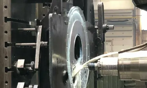 Broche d'alésage en train d'aléser une pièce à bride, arrosée de liquide de coupe